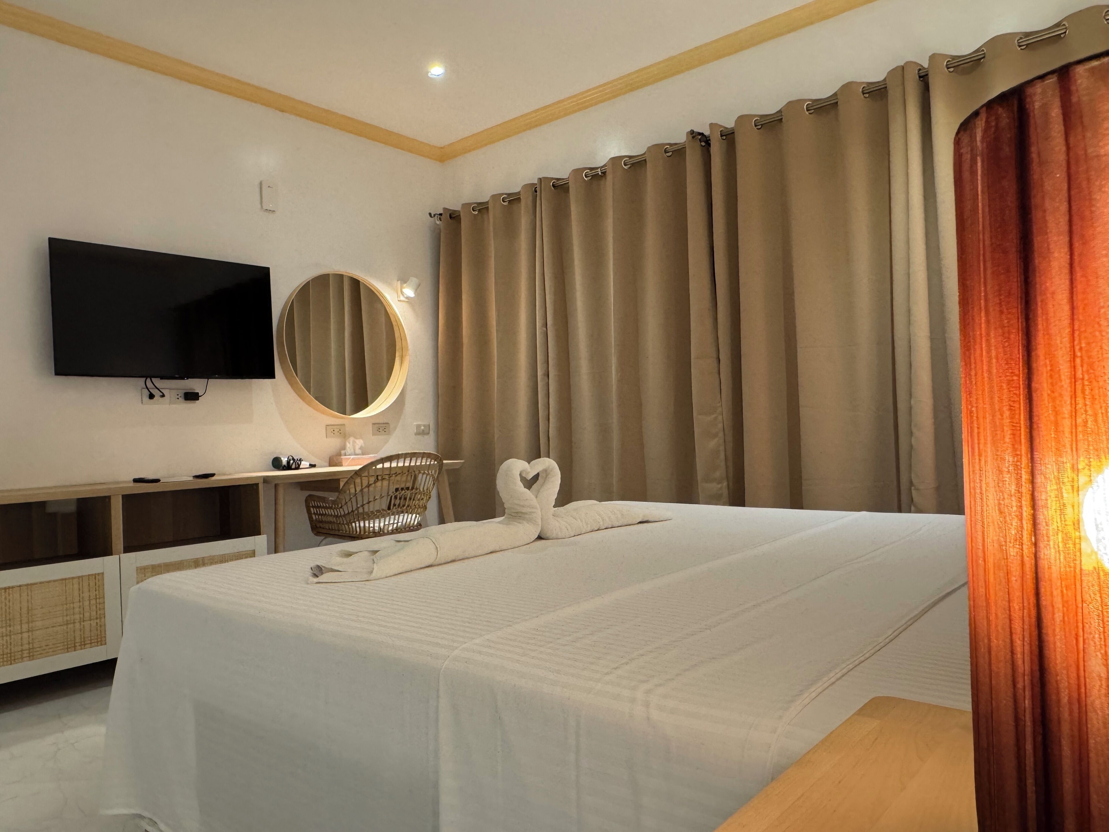 Habitación de hotel con cama, televisión, escritorio con silla, espejo y cortinas.
