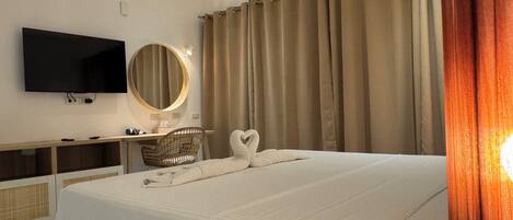 A hotel room with a bed, a TV, a desk with a chair, a mirror, and curtains.