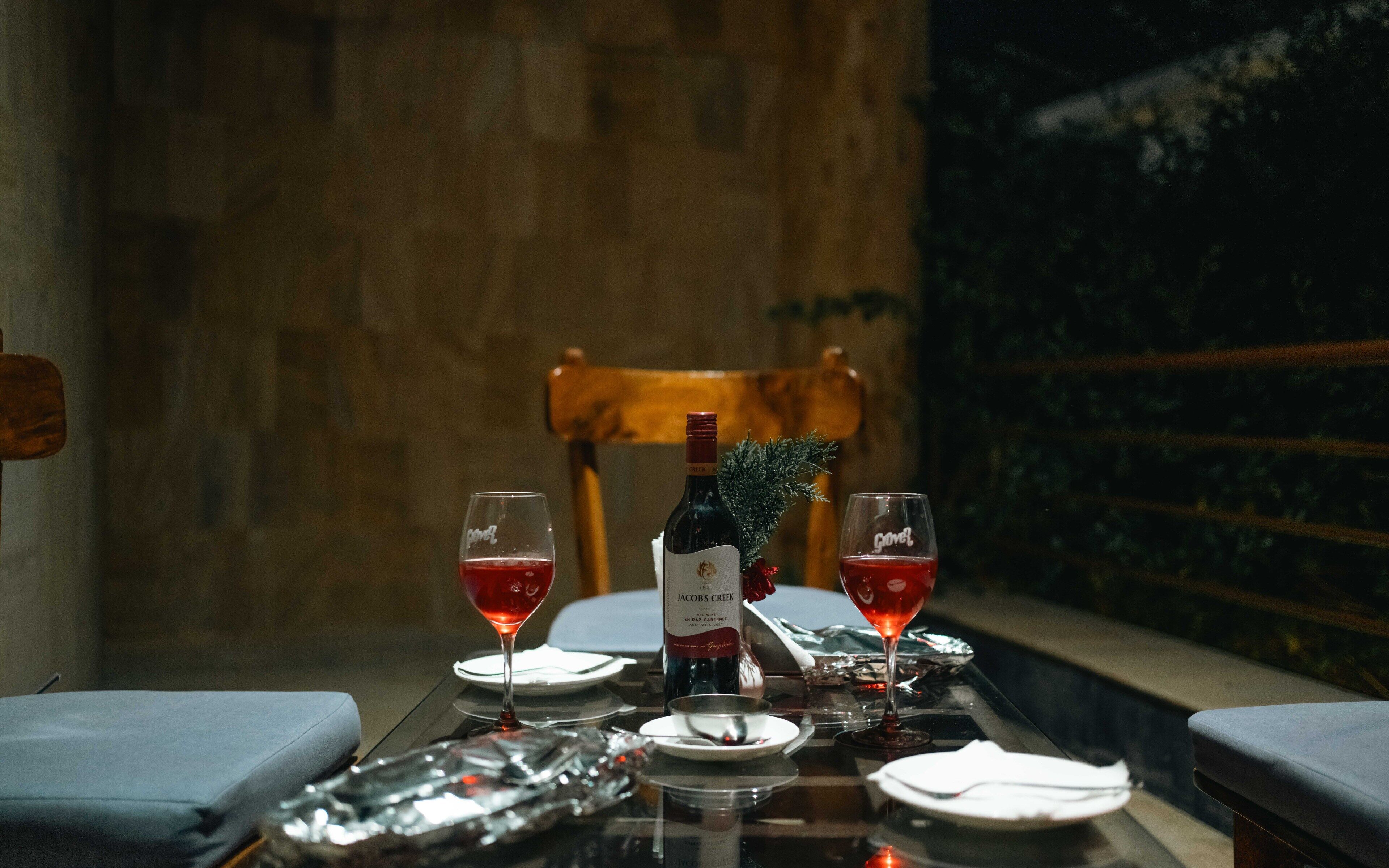 A dining table set with two wine glasses, a bottle of wine, and a small plant.