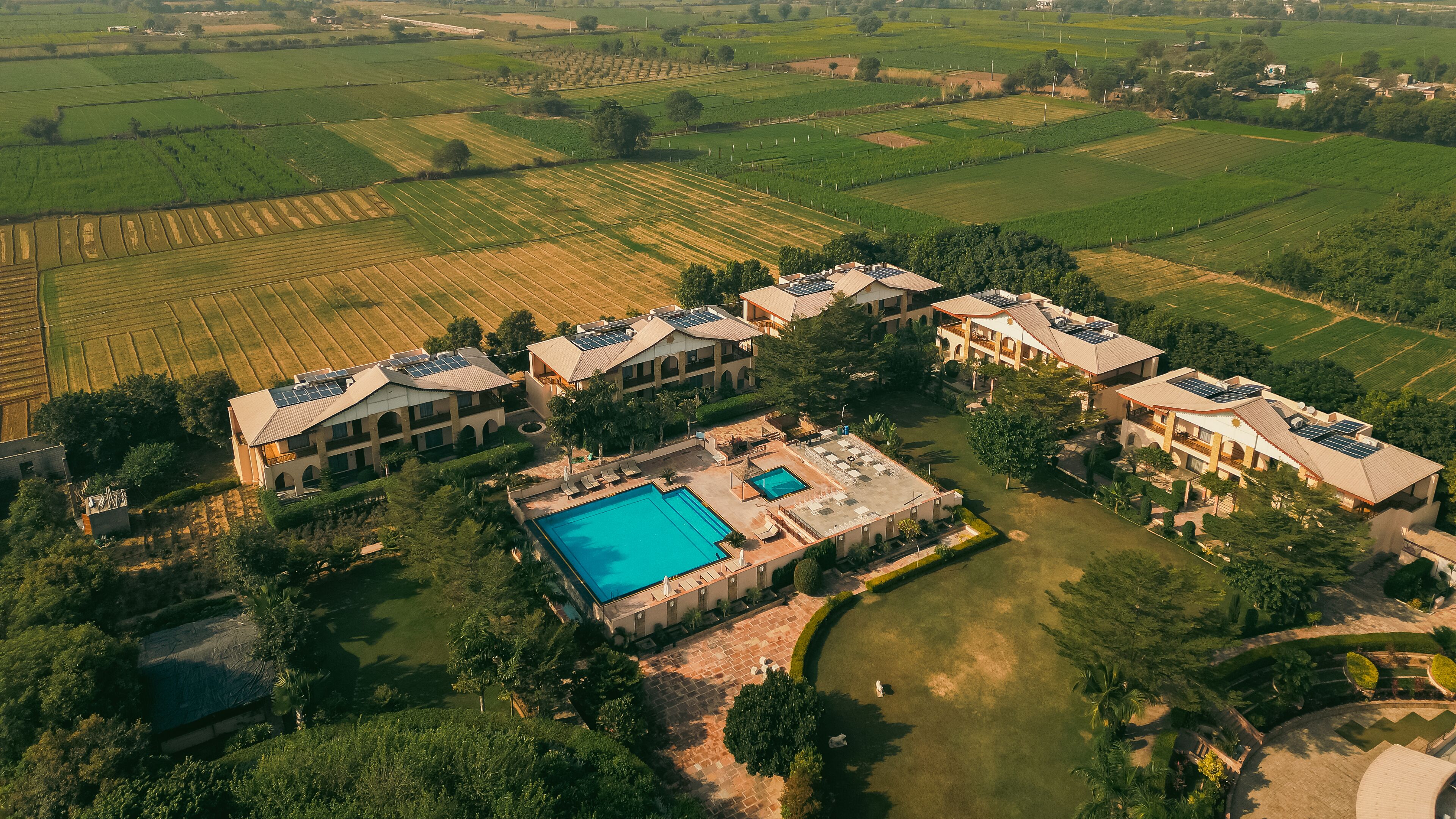 An aerial view of a resort with multiple buildings, a swimming pool, and surrounding agricultural fields.