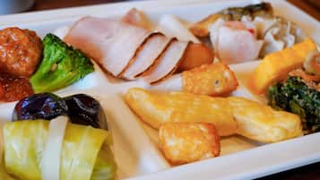 A white rectangular plate with various food items including slices of ham, broccoli, and other vegetables.