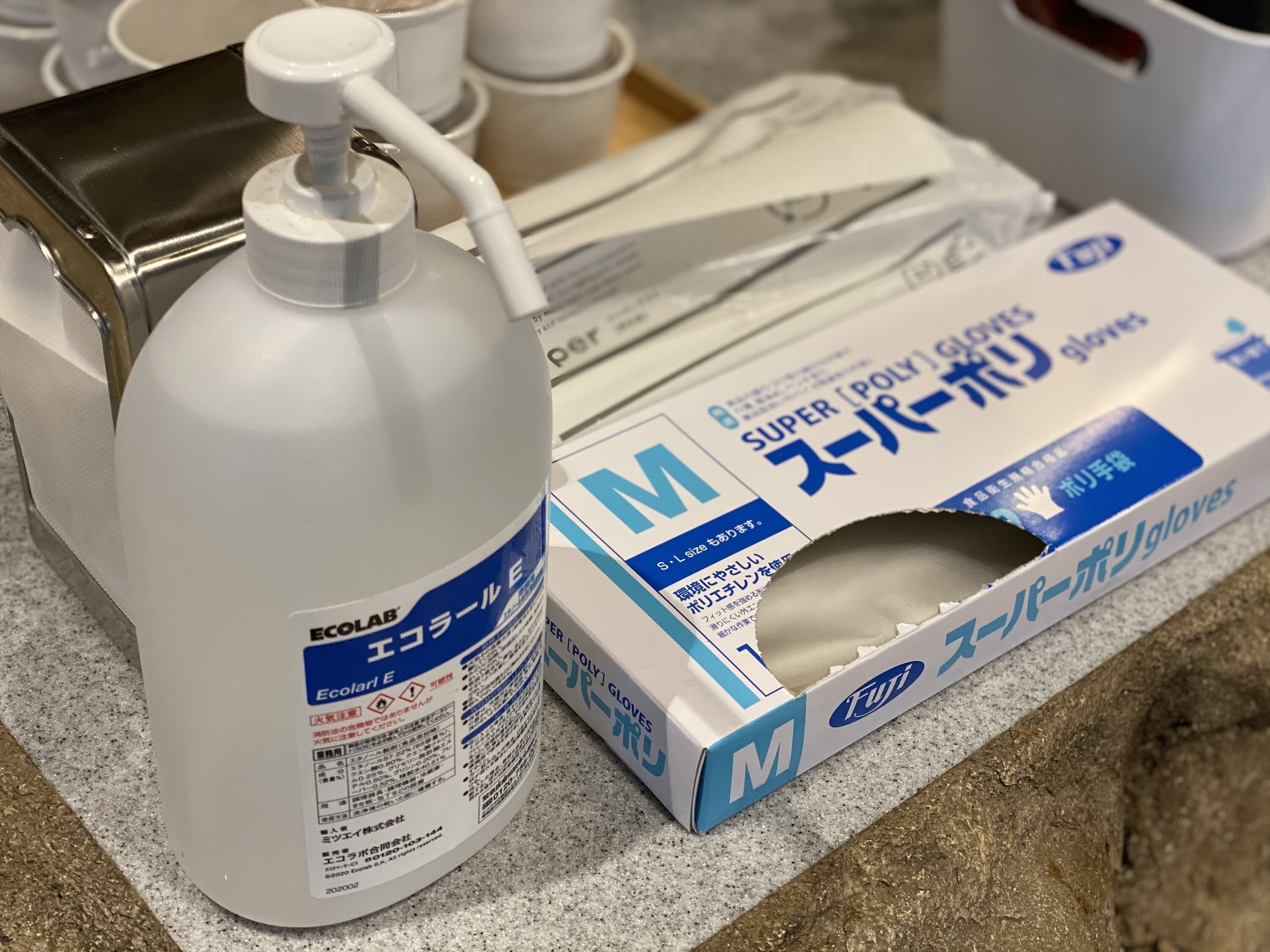 A white plastic bottle with a pump, a box of gloves, and a metal container on a countertop.