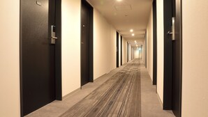 Un pasillo de hotel con pisos alfombrados, puertas negras e iluminación empotrada.