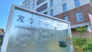 Señal de Henn na Hotel con un edificio moderno al fondo.