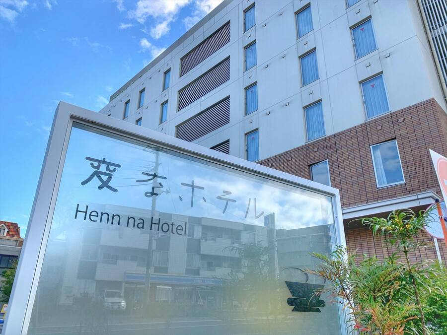 Señal de Henn na Hotel con un edificio moderno al fondo.