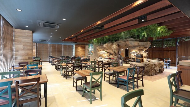 Un restaurante con mesas y sillas de madera, una formación rocosa como centro de mesa y un mural en la pared.