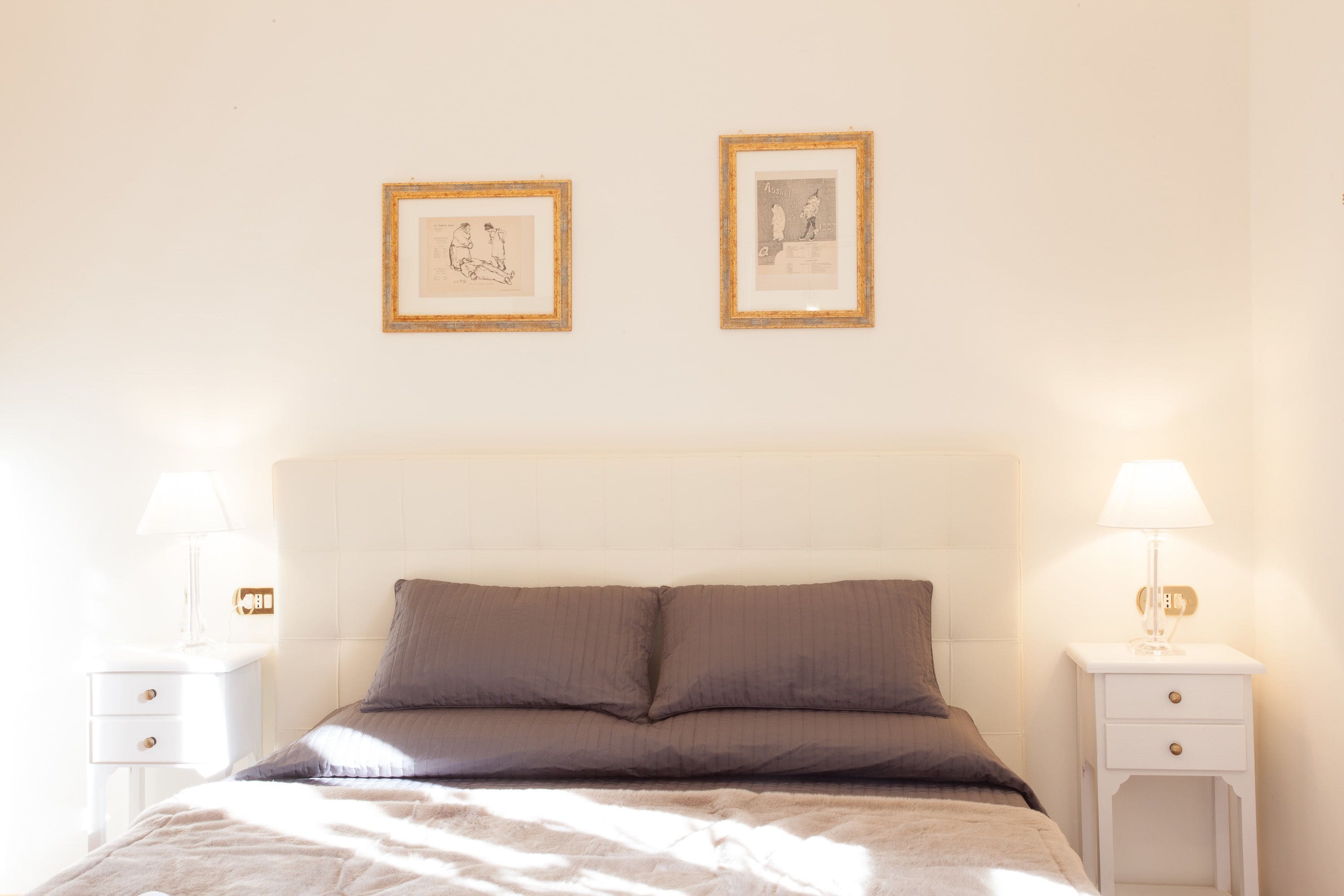 A neatly arranged bedroom with a bed, two bedside tables, and two framed pictures on the wall.