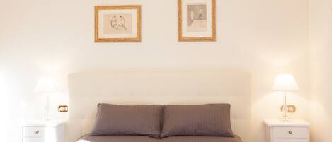 A neatly arranged bedroom with a bed, two bedside tables, and two framed pictures on the wall.