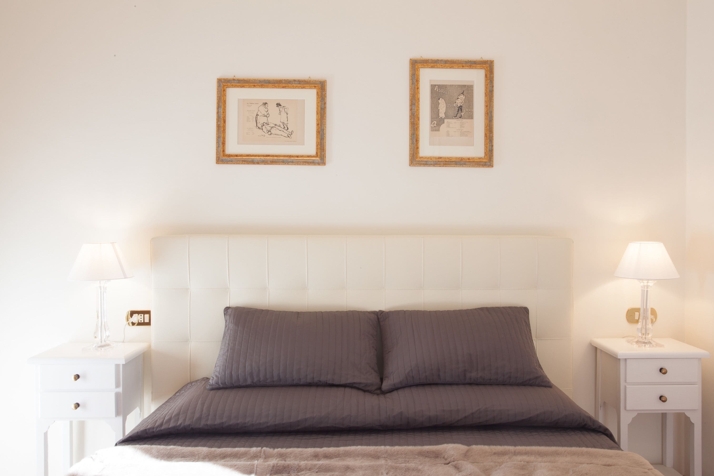Ein ordentlich eingerichtetes Schlafzimmer mit einem großen Bett, zwei Nachttischen und zwei gerahmten Bildern an der Wand.