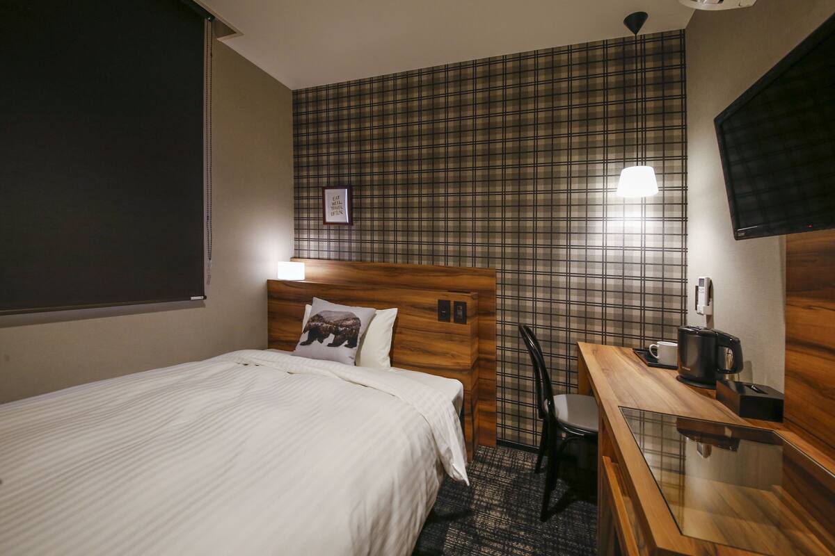 A hotel room with a bed, a wooden desk, a chair, a coffee maker, and a TV mounted on the wall.