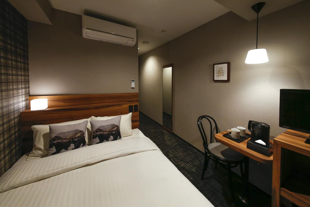 A hotel room with a bed, bedside table, chair, and a TV.