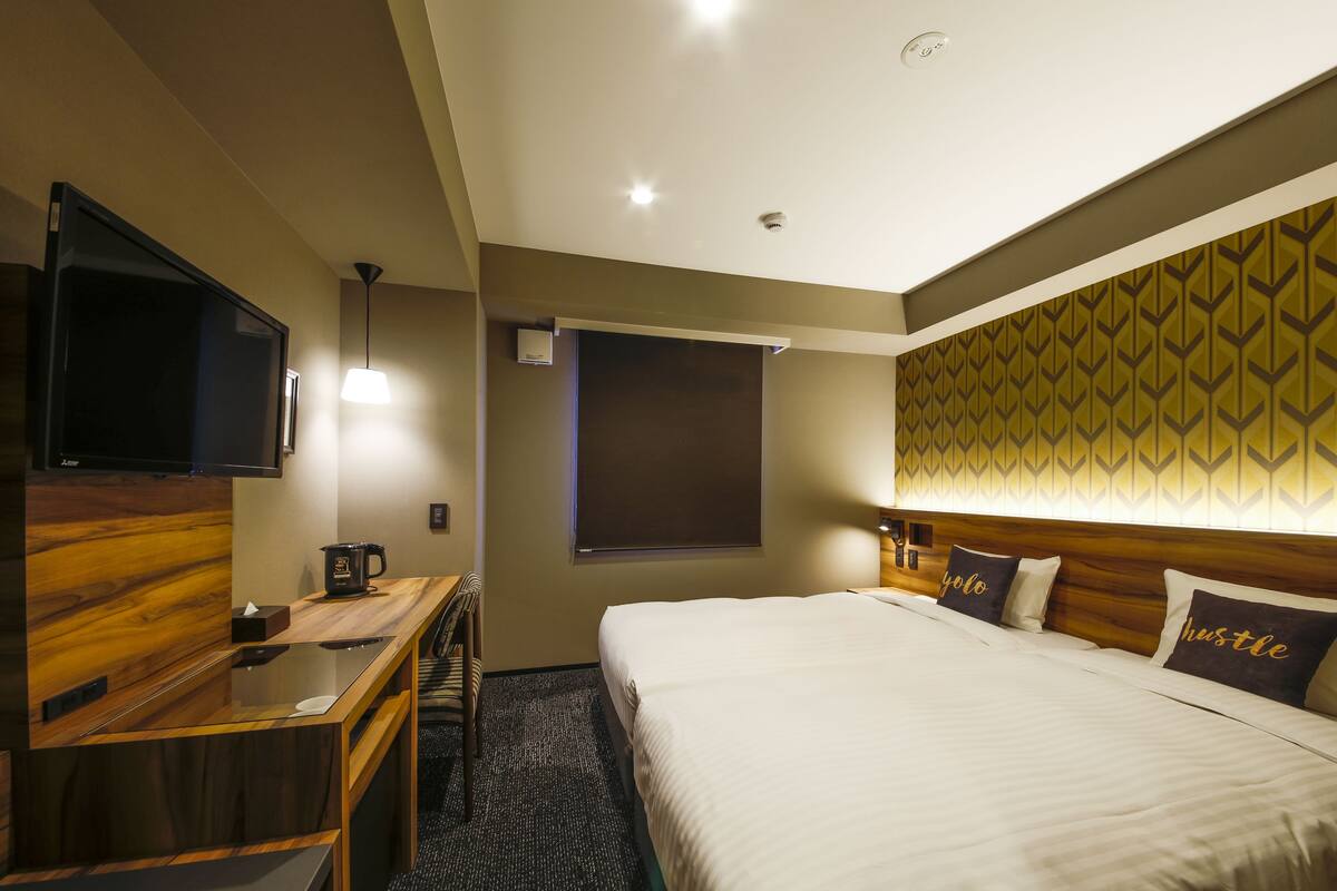 A hotel room with a bed, a desk, a television, and a window.