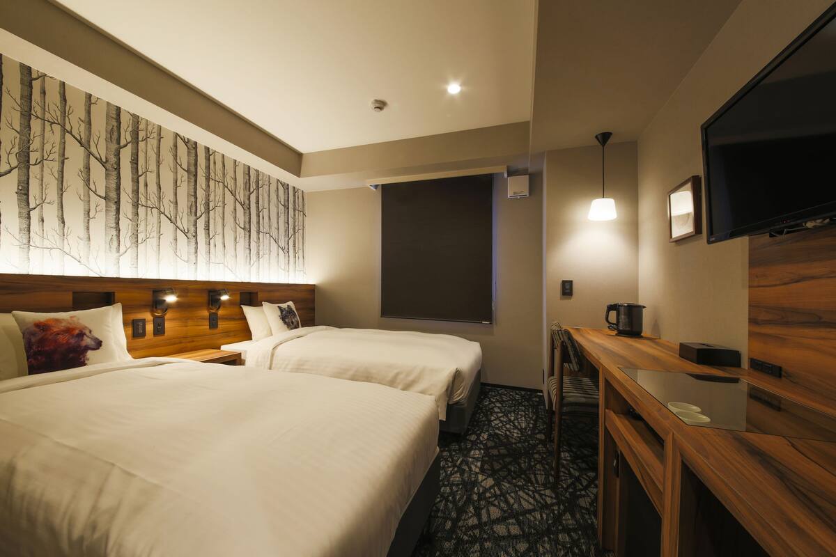 A hotel room with two beds, a wooden headboard, a flat-screen TV, a desk, and a large window.