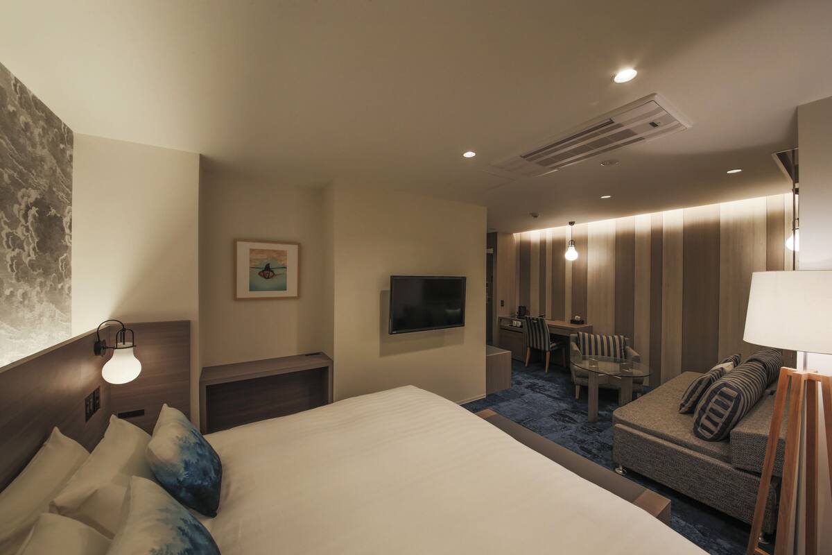 A hotel room with a large bed, a sofa, a desk, and a TV.