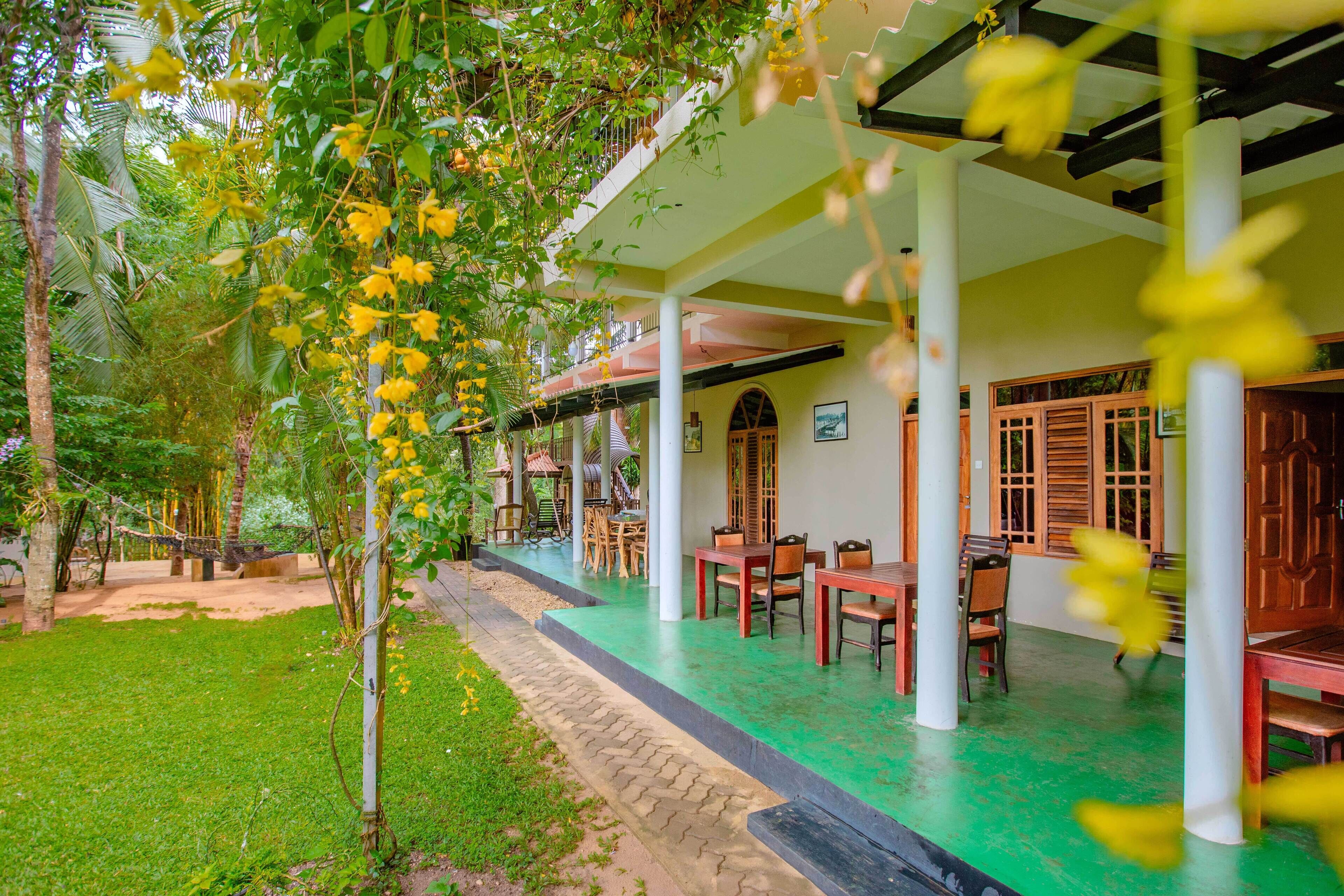 A covered outdoor area with a green floor, white columns, and wooden furniture.