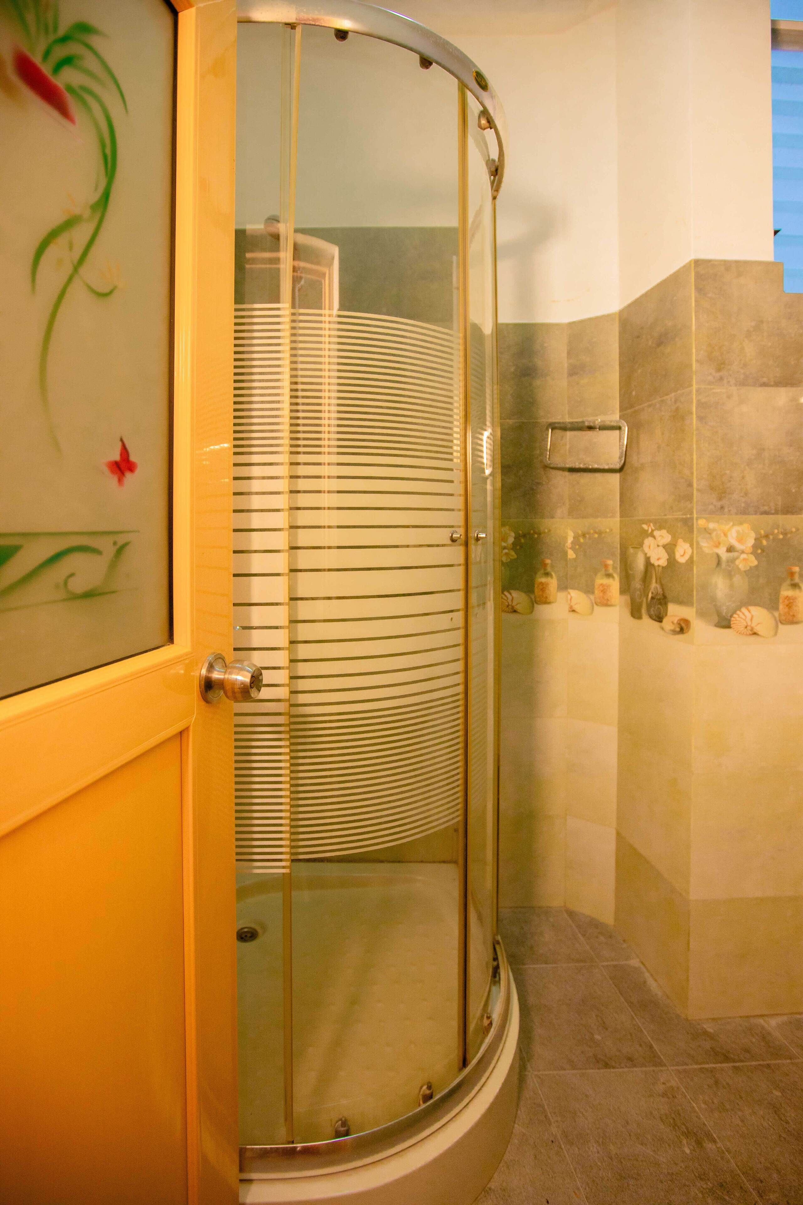 Cabina de ducha con puerta de vidrio, toallero y pared revestida de azulejos decorativos.