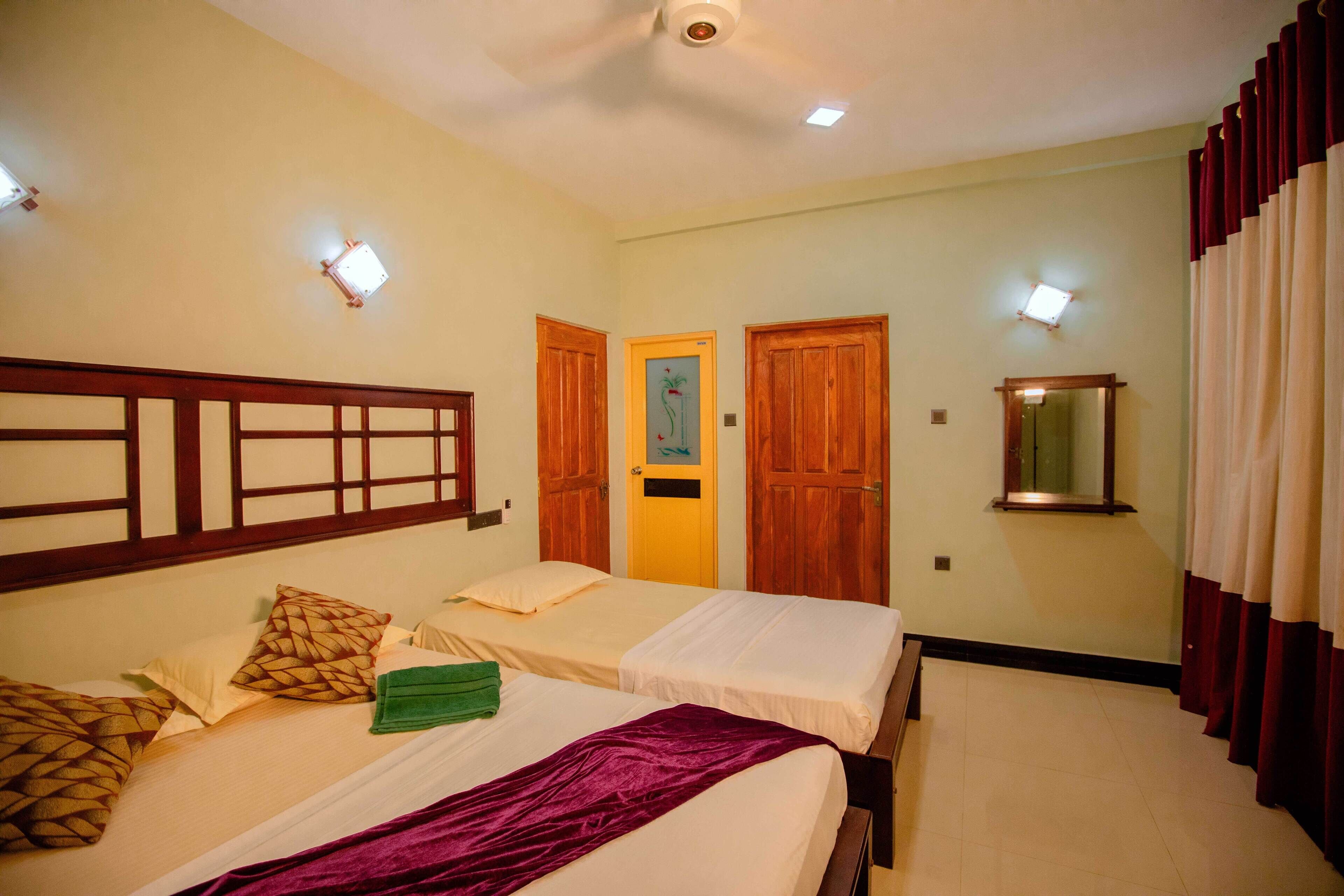 A hotel room with two beds, wooden headboards, a mirror, and a door with a picture frame.