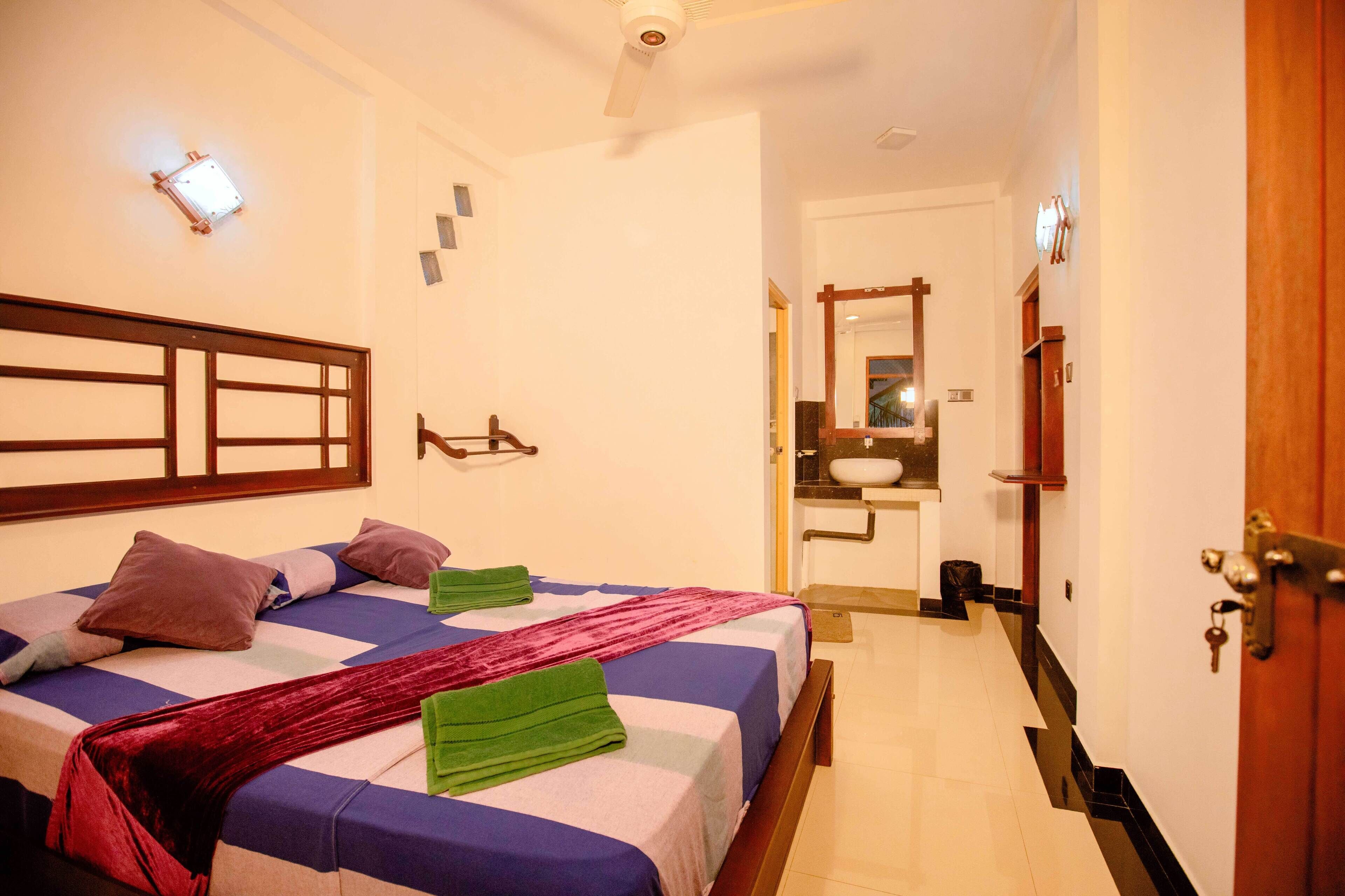 A hotel room with a bed, a bathroom with a sink and mirror, and a door.