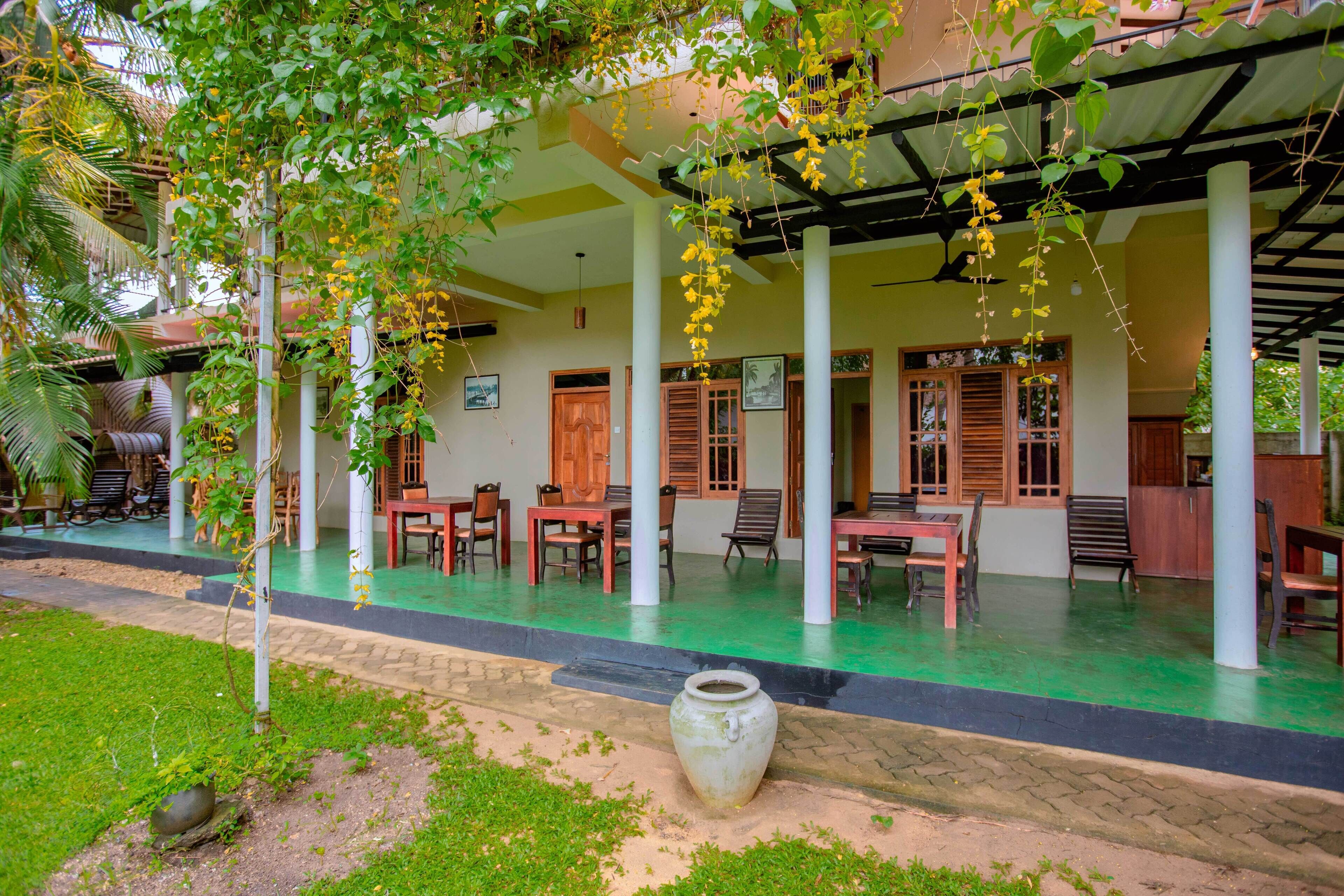 Un espacio al aire libre cubierto con mesas y sillas, un gran jarrón decorativo y un césped verde.