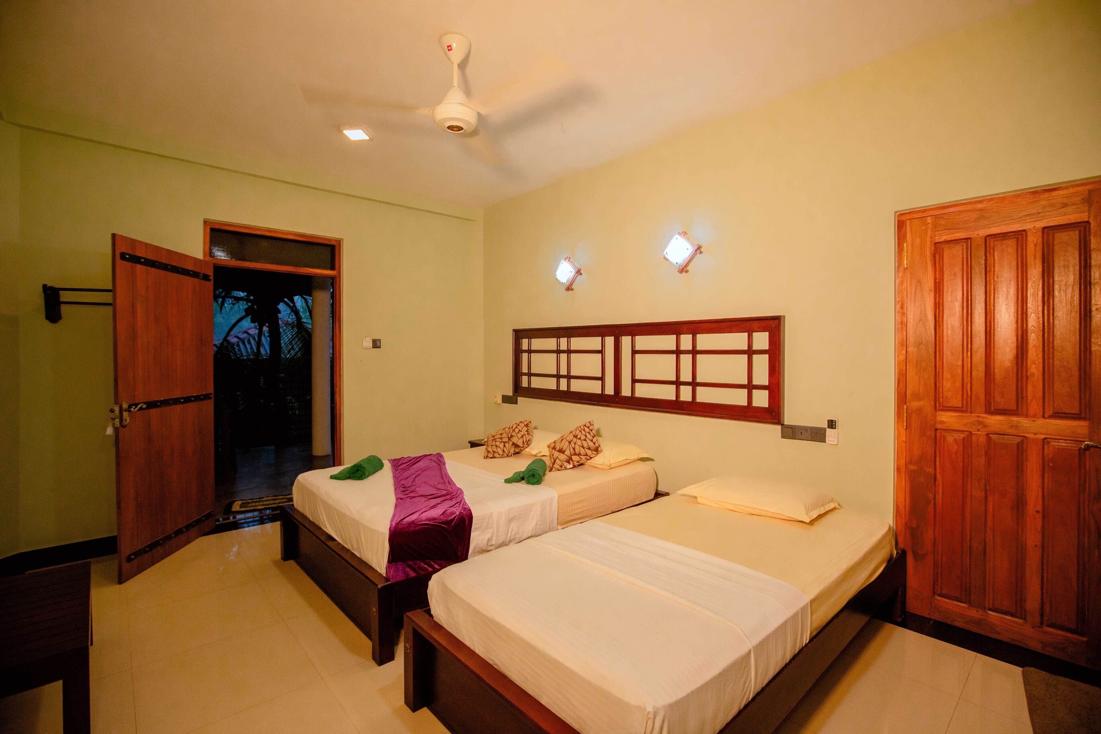 A hotel room with two beds, a wooden wardrobe, a ceiling fan, and a door leading outside.