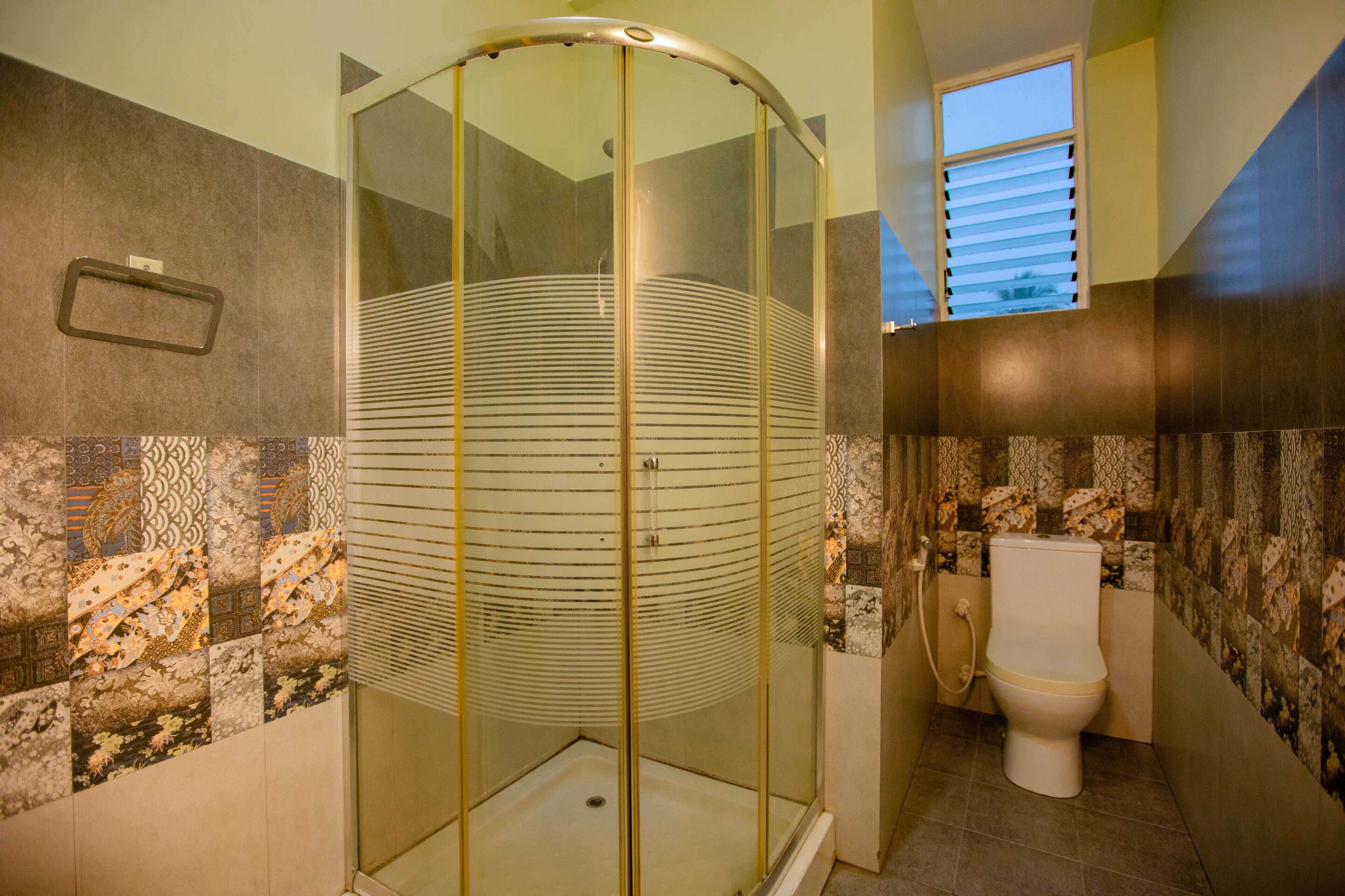 A bathroom with a glass-enclosed shower, a toilet, and patterned tiles on the walls.