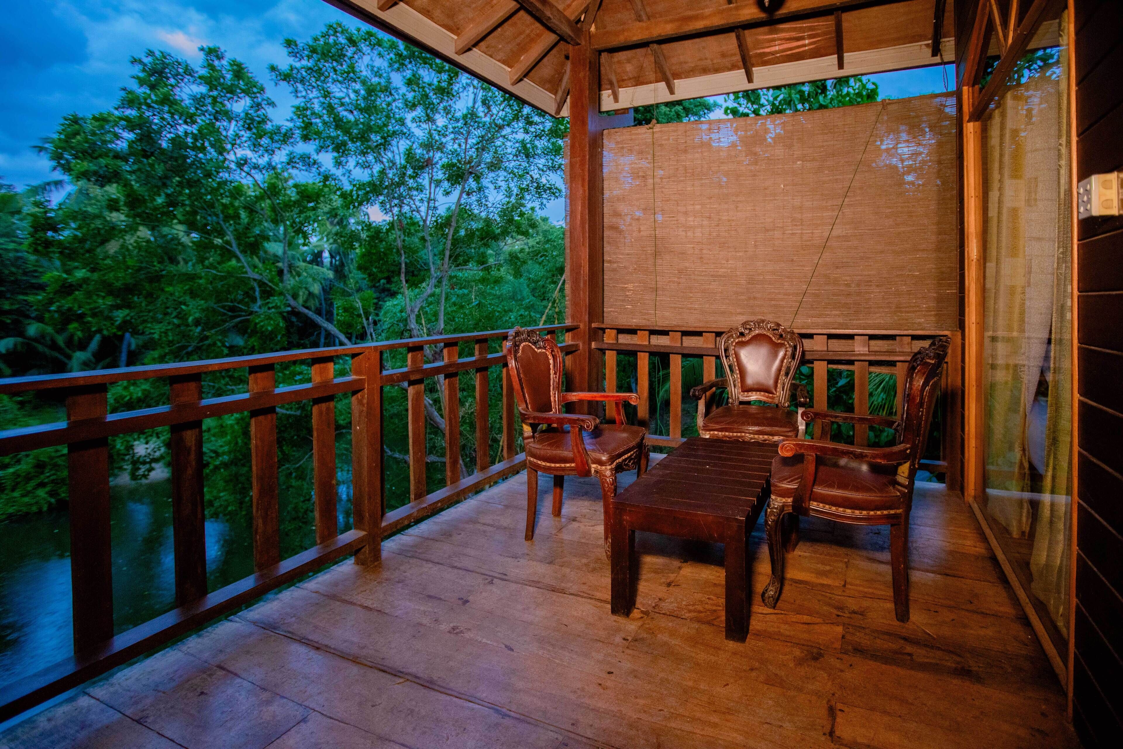 A wooden deck with a table and chairs, overlooking a body of water and surrounded by trees.