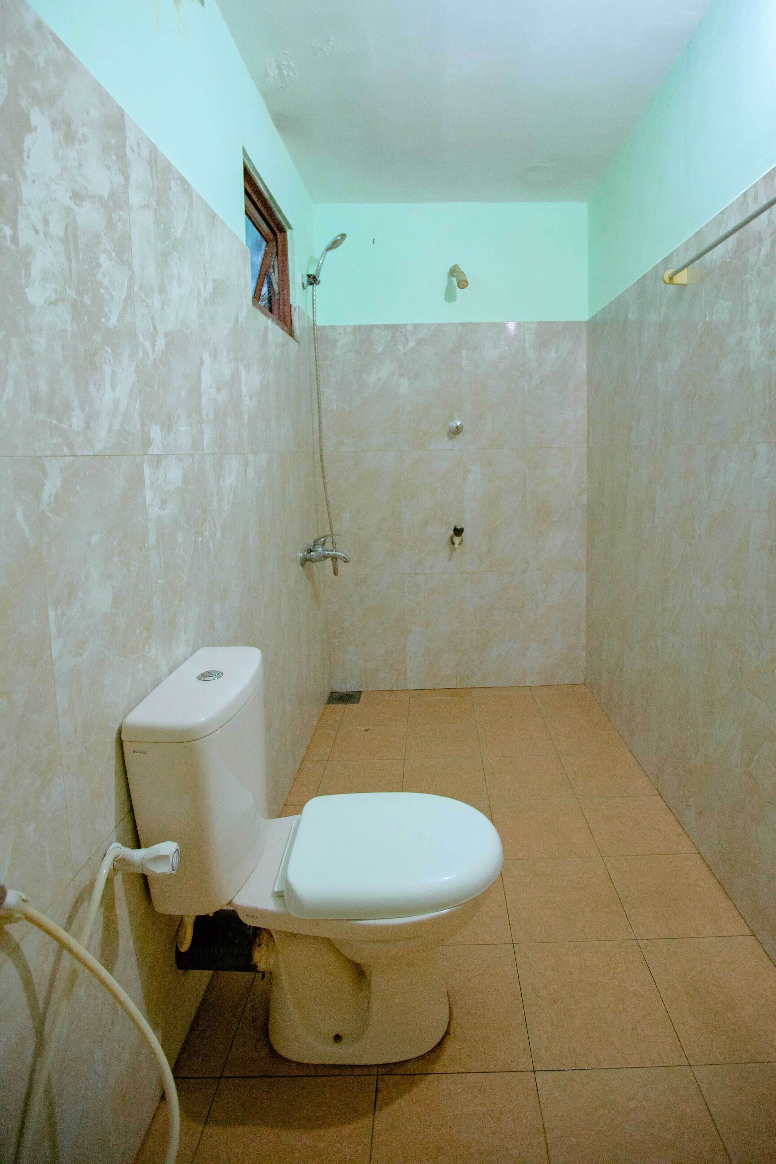 A small, tiled bathroom with a toilet, a shower, and a window.