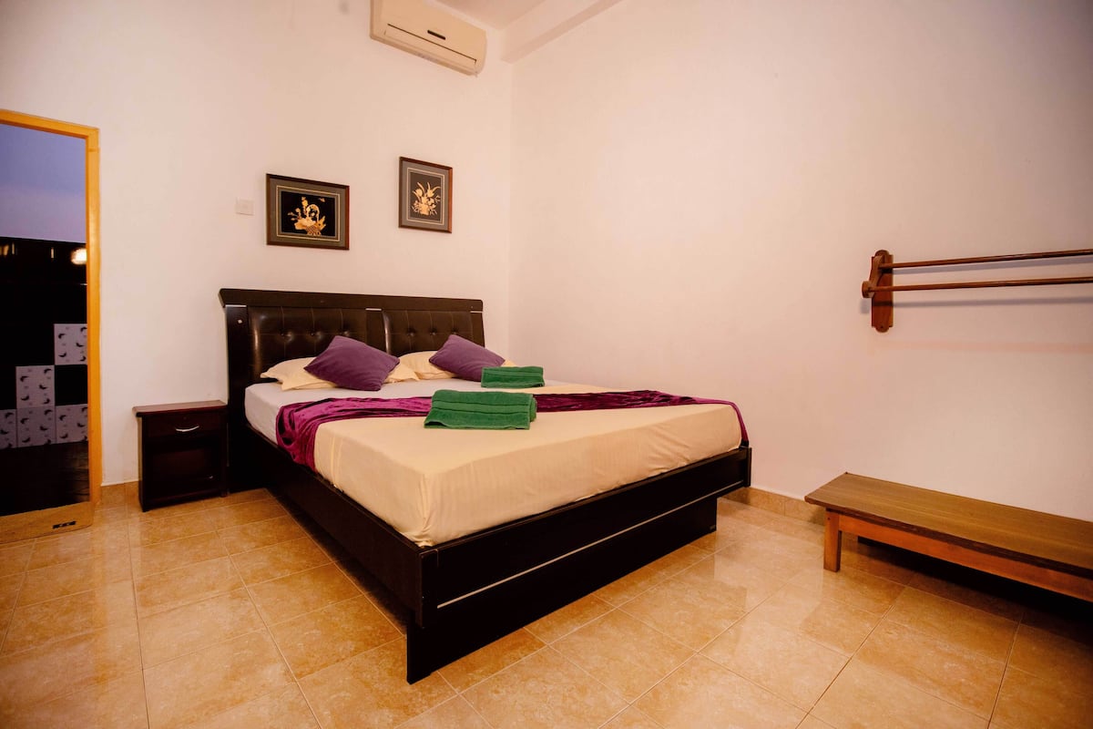A bedroom with a bed, nightstands, a bench, and two framed pictures on the wall.