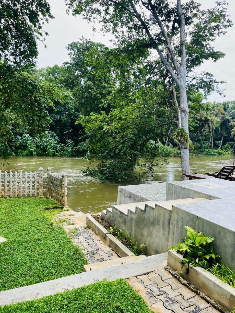 Une promenade le long de la rivière, avec un banc en béton, une zone herbeuse et une clôture en bois.