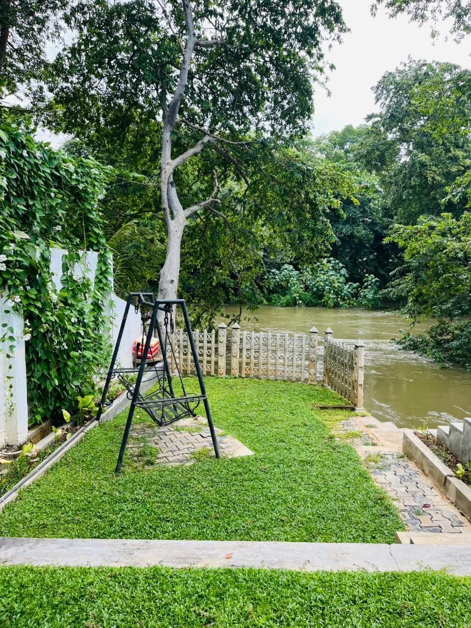 A garden with a swing set, a white fence, and a river.