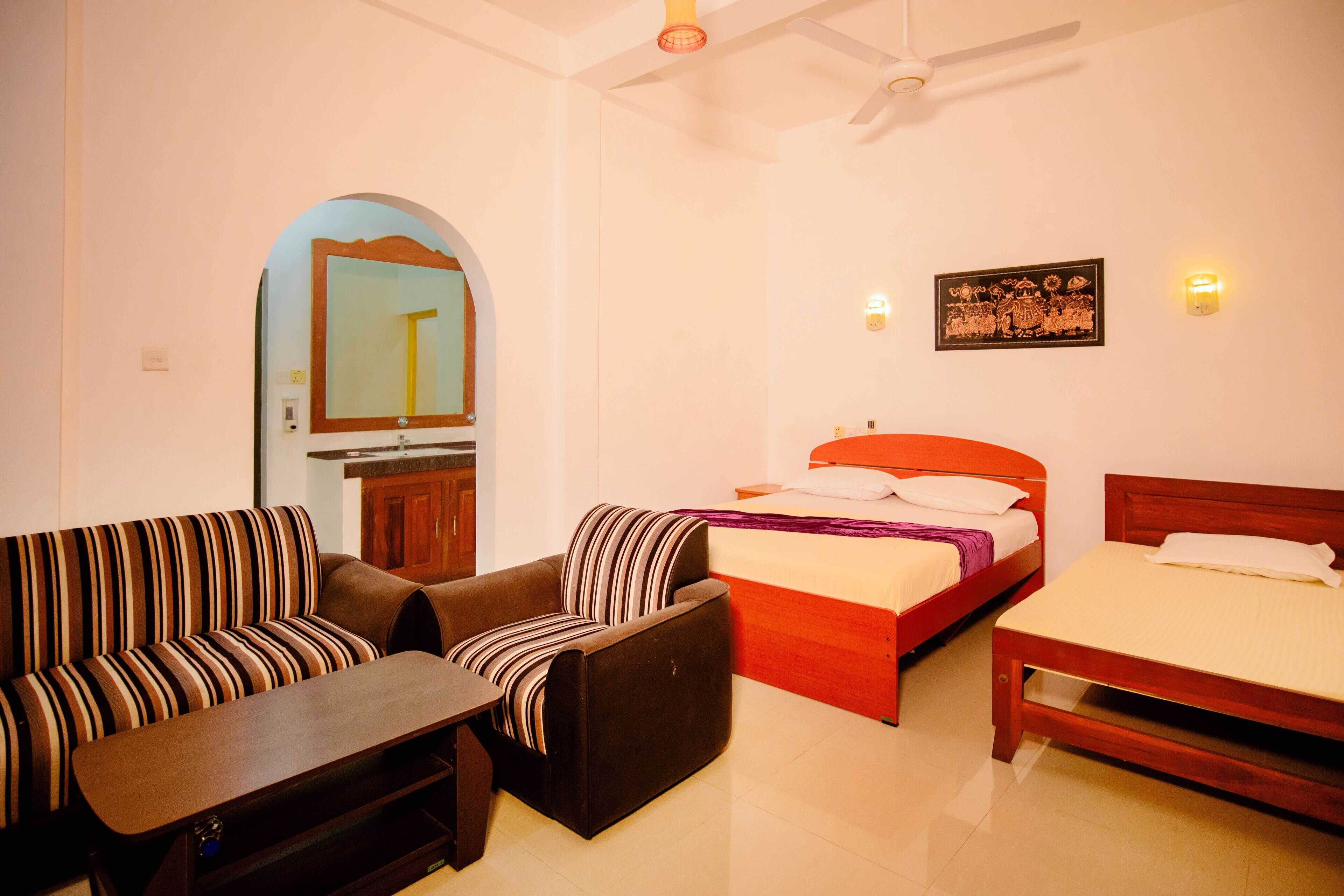 A hotel room with a sofa, a chair, a bed, a small table, and a mirror.