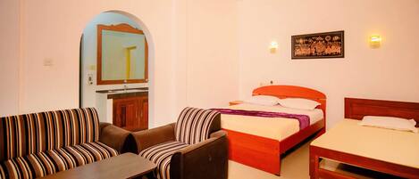 A hotel room with a sofa, a chair, a bed, a small table, and a mirror.