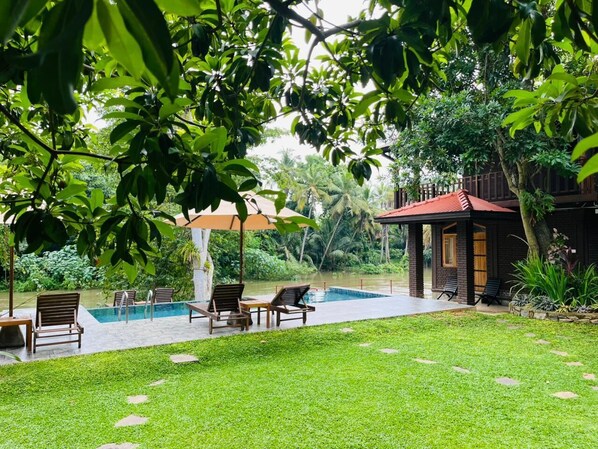Área da piscina com espreguiçadeiras, um espaço de estar coberto e um edifício com telhado vermelho.