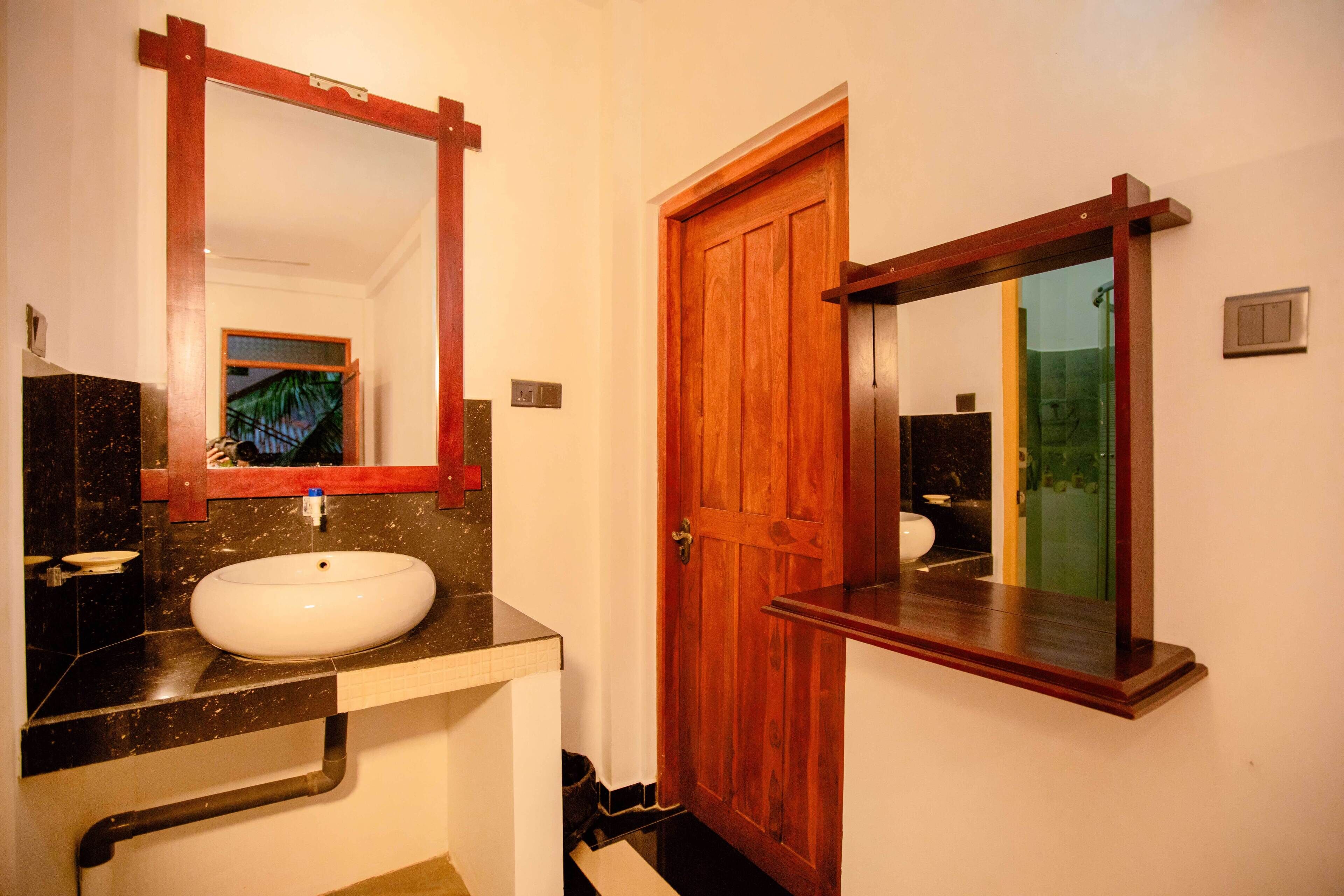 Un baño con lavamanos blanco, puerta de madera y espejo.