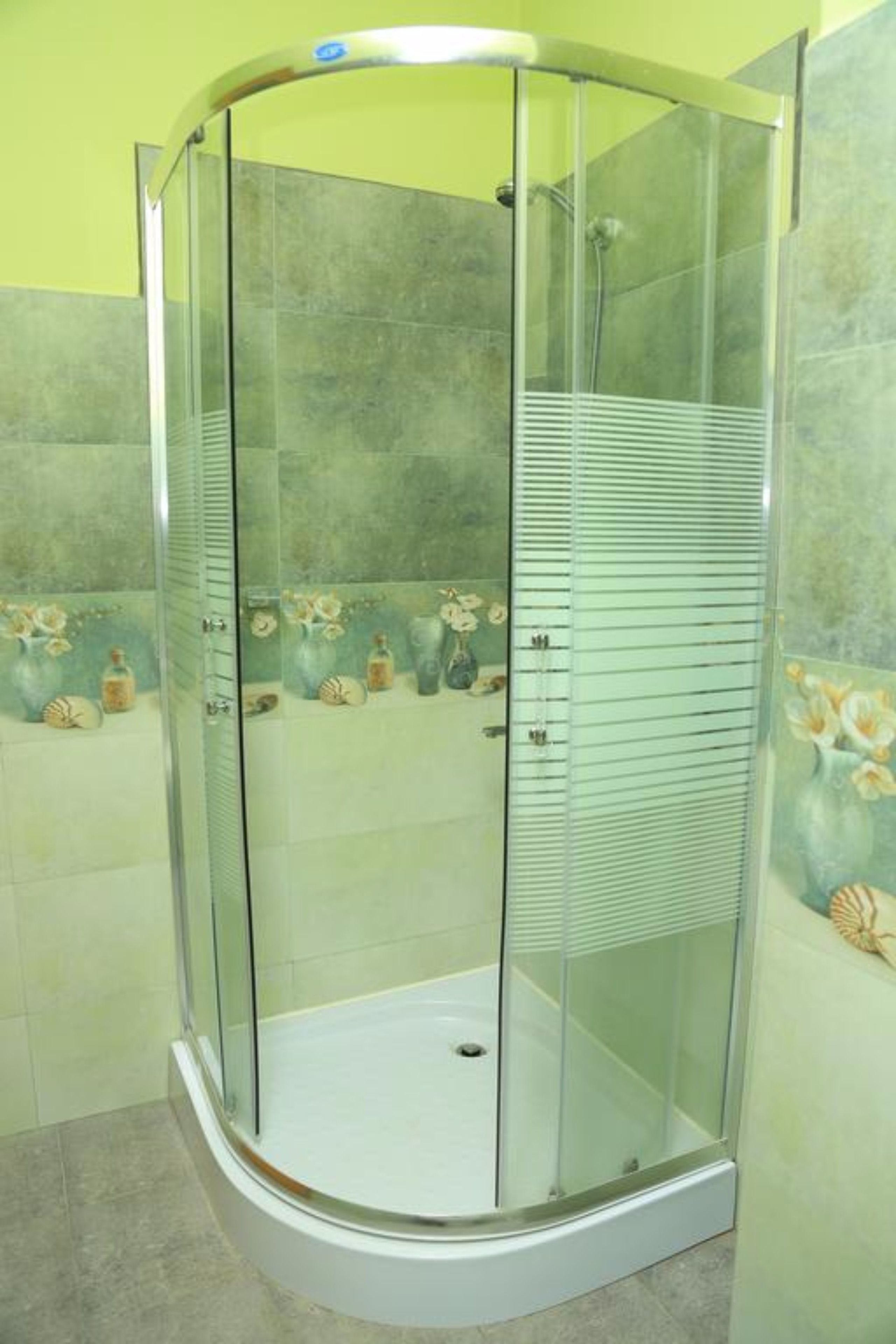 A glass-enclosed shower stall with a curved design, tiled walls, and decorative tiles with floral patterns.