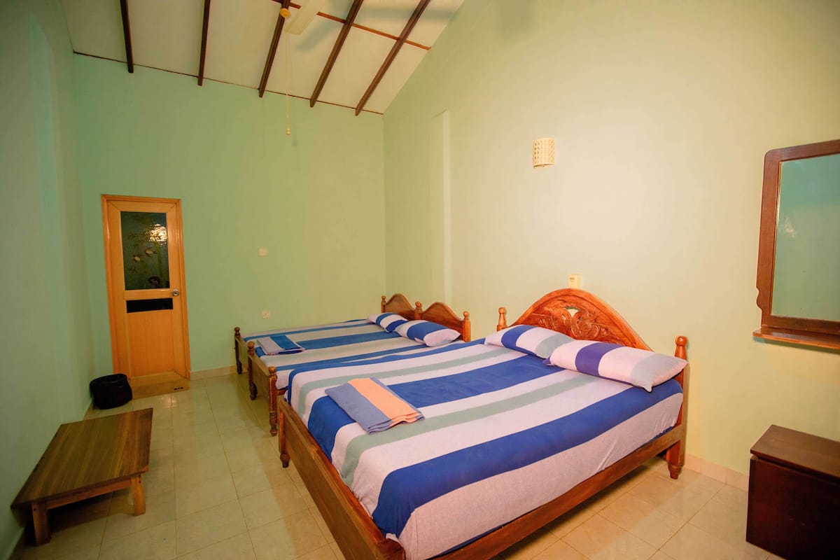 A room with three wooden beds, each with blue and white striped bedding. There is a wooden bench and a small table.