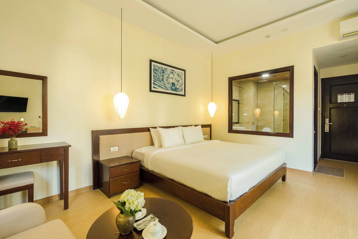 A hotel room with a large bed, bedside tables, a desk, a chair, and a round table with a vase of flowers.