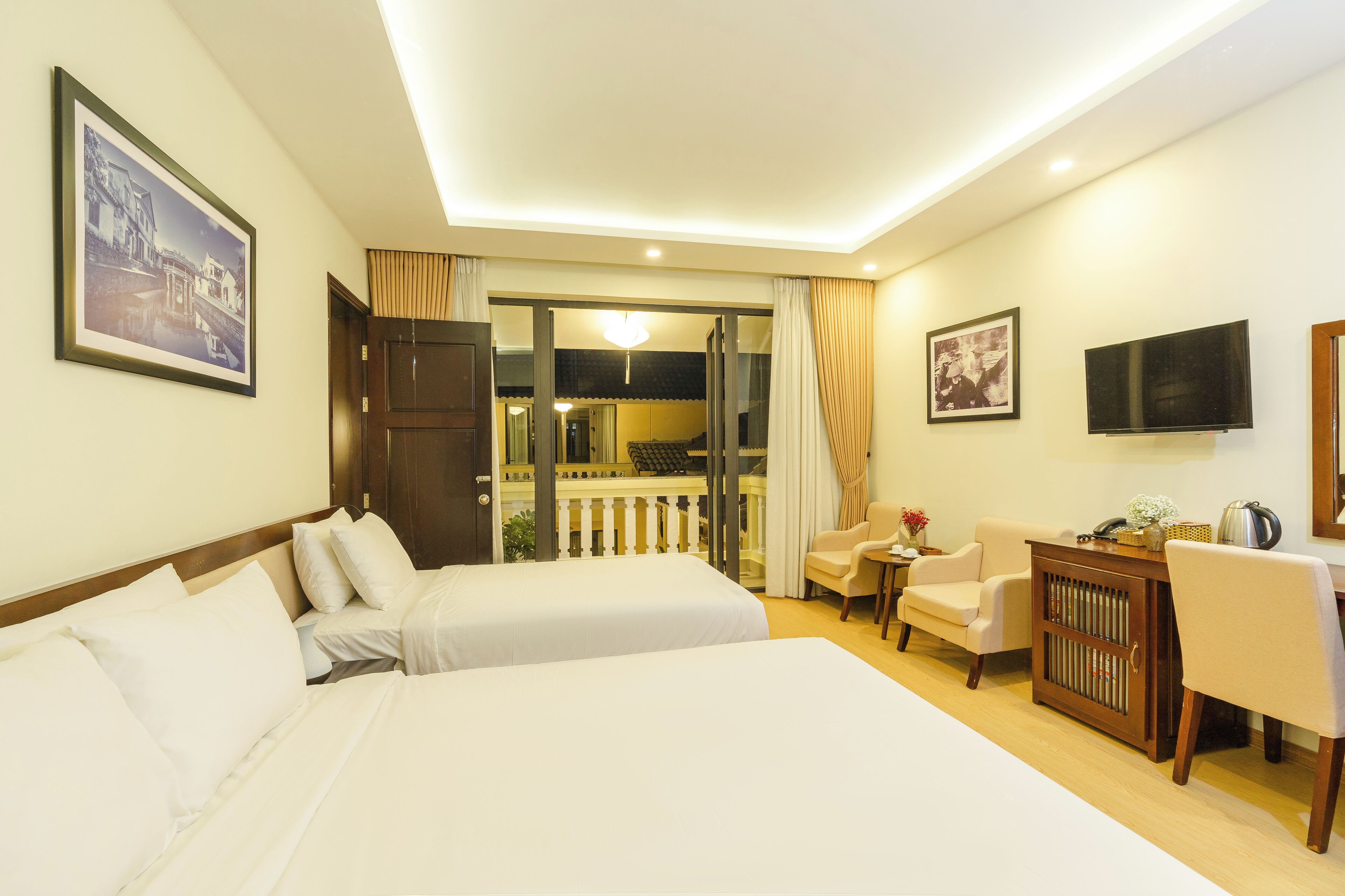 A hotel room with two beds, a desk, a chair, a TV, and a balcony with a railing.