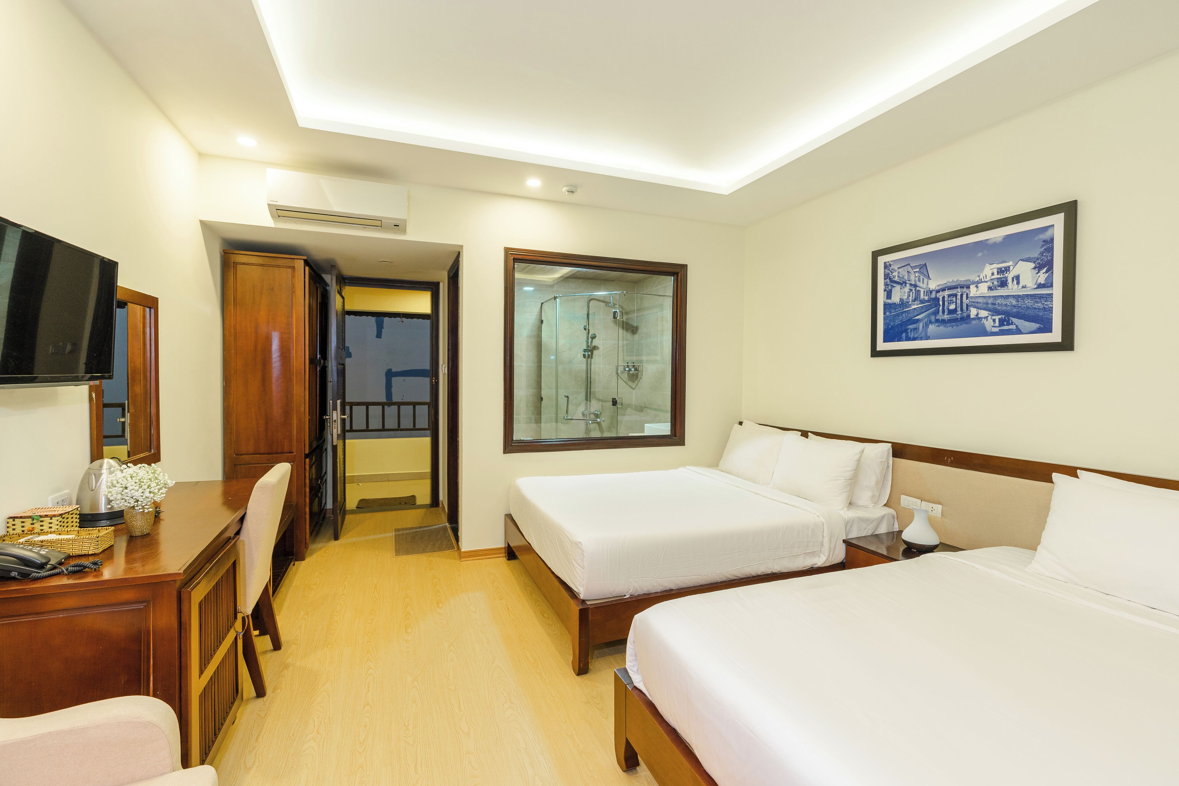 A hotel room with two beds, a desk with a chair, a television, and a framed picture on the wall.