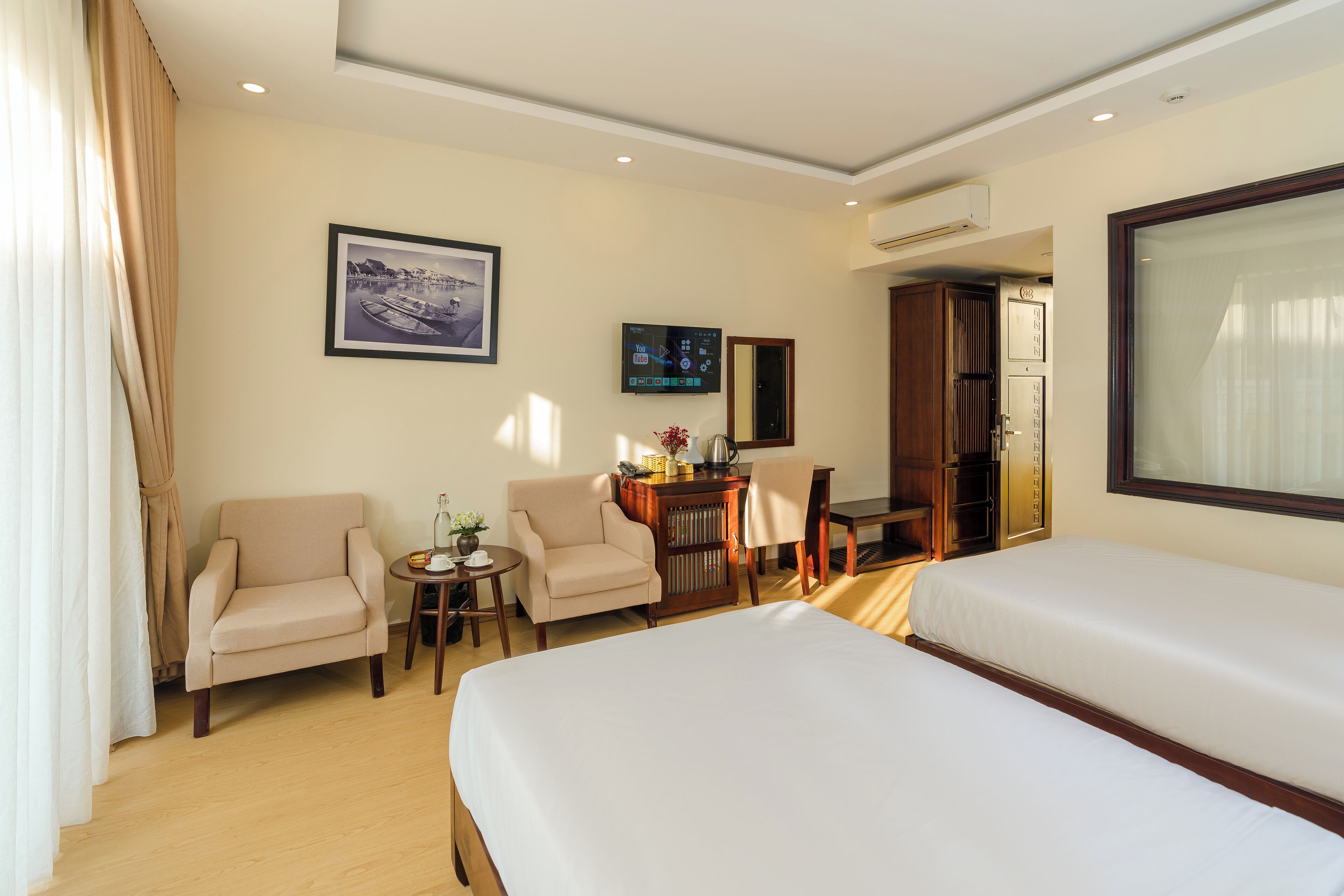 A hotel room with two beds, a desk, a chair, and a small table.