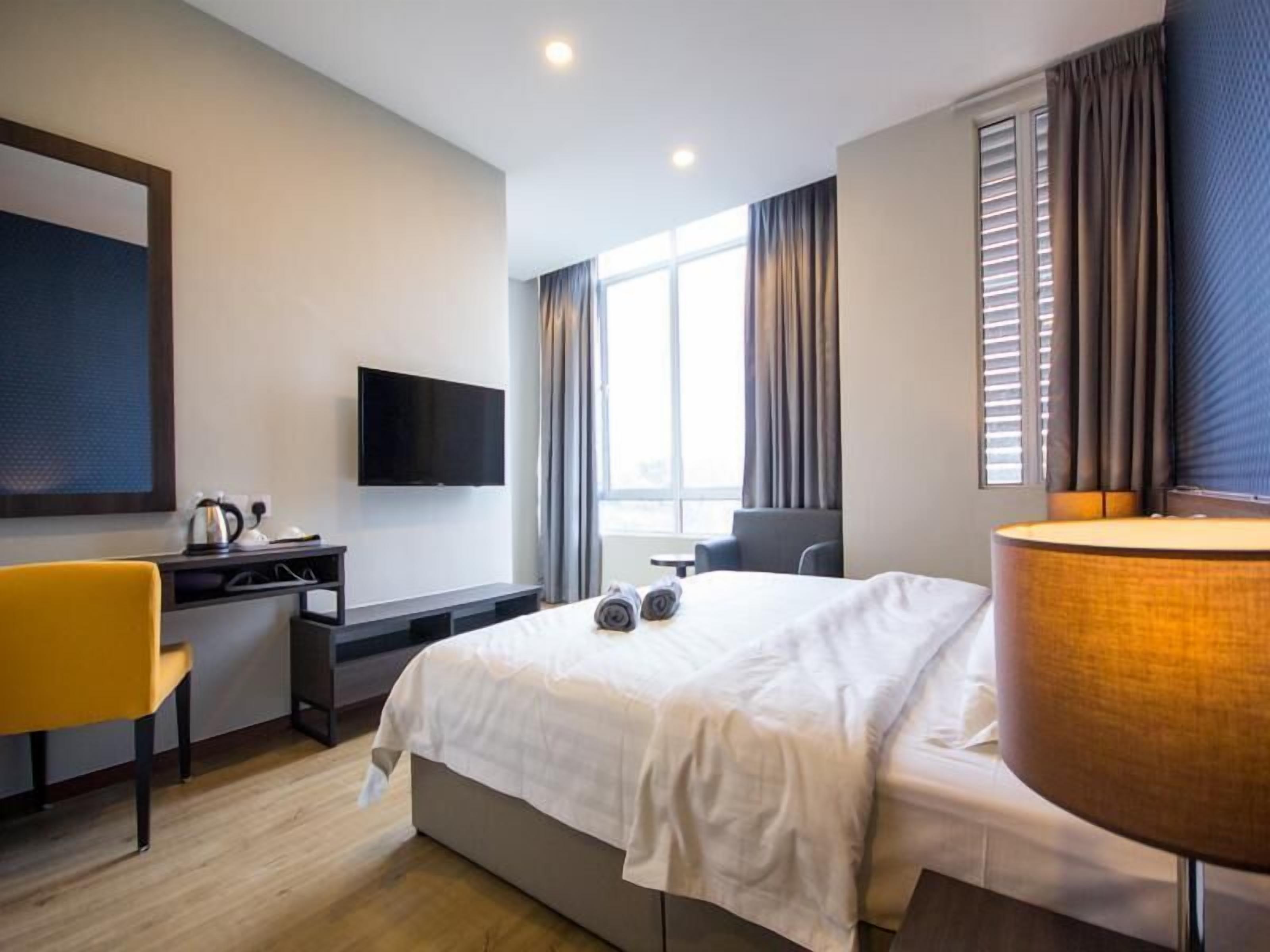 Una habitación de hotel con una cama, un escritorio con televisor de pantalla plana, una silla y una lámpara.