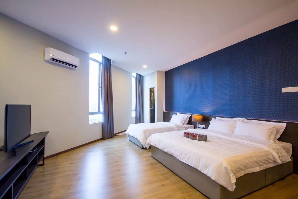 A hotel room with two beds, a flat-screen TV, an air conditioning unit, and a large window with curtains.