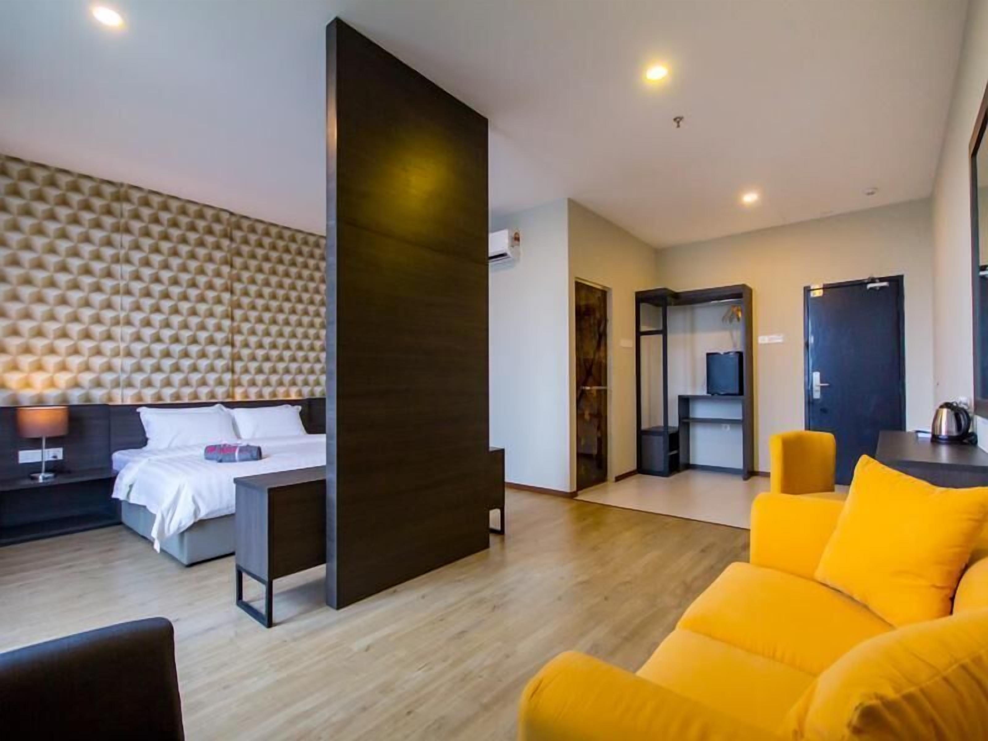 A modern hotel room with a bed, a desk, a sofa, and a wall with a geometric pattern.