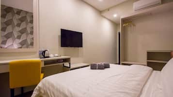 Habitación de hotel con cama, escritorio con silla, televisor de pantalla plana, armario y pared con un diseño geométrico.
