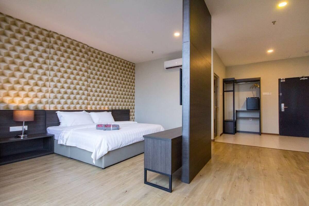 A modern hotel room with a geometric patterned headboard, a bed with white linens, a bedside table, and a built-in wardrobe.