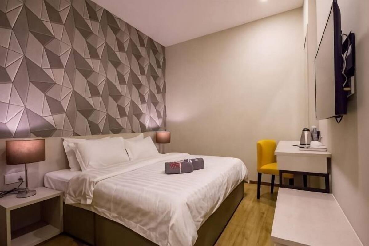 A hotel room with a bed, bedside table, lamp, chair, desk, and a wall with geometric patterns.