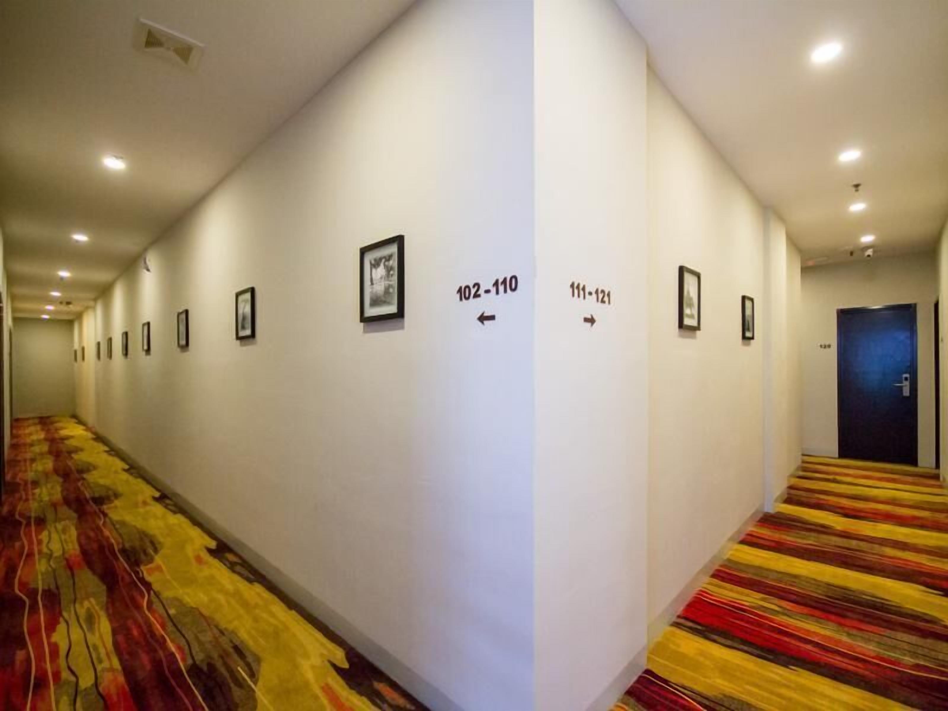 Ein Hotelgang mit nummerierten Türen, Teppichböden und gerahmten Bildern an den Wänden.