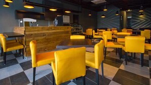 A modern restaurant interior with checkered flooring, yellow chairs, and pendant lighting. - OMG Hotel (Simpang Ampat)