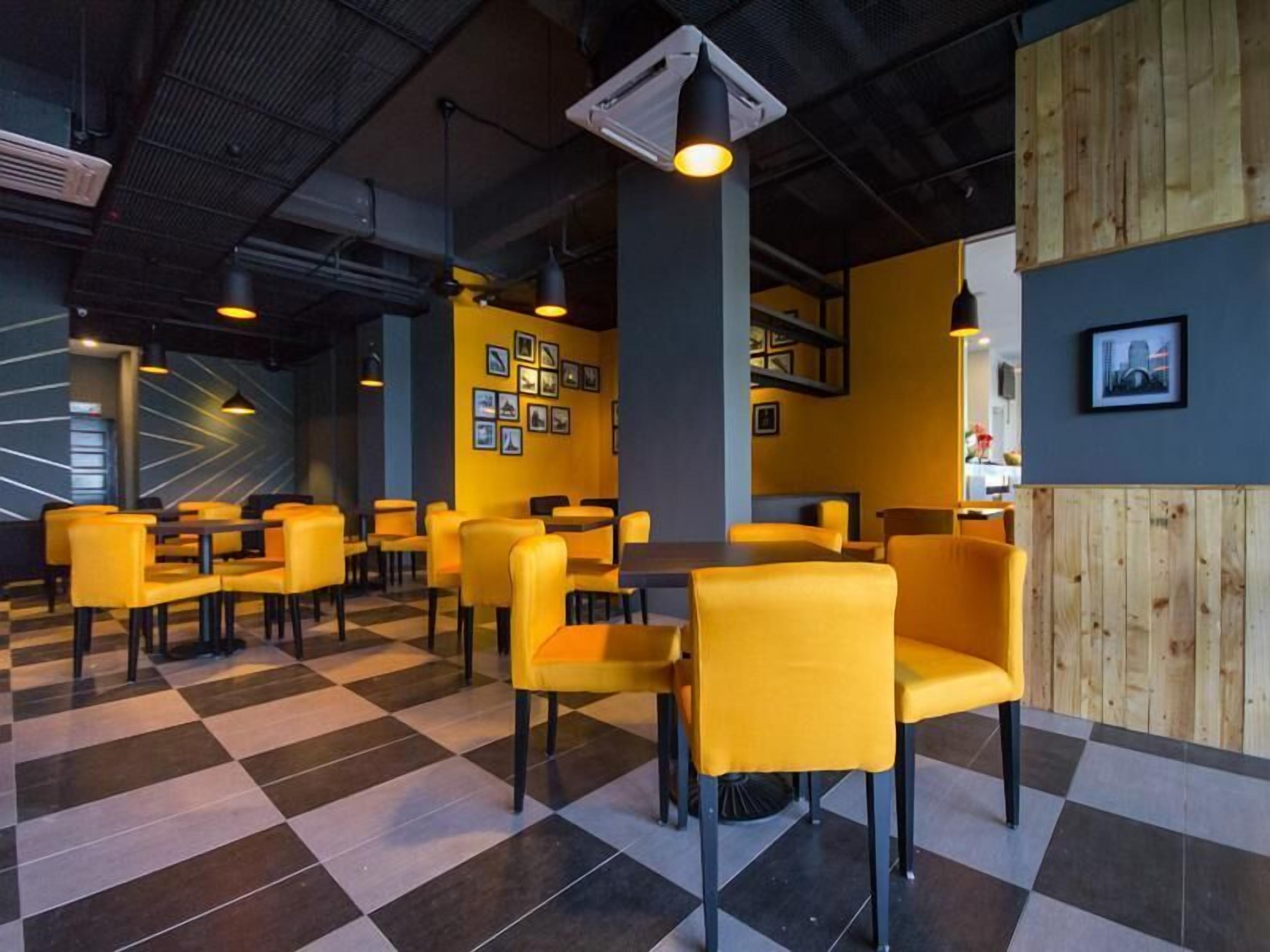 A modern restaurant interior with yellow chairs and tables, checkered flooring, and framed pictures on the walls.