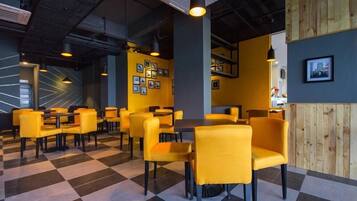 A modern restaurant interior with yellow chairs and tables, checkered flooring, and framed pictures on the walls.